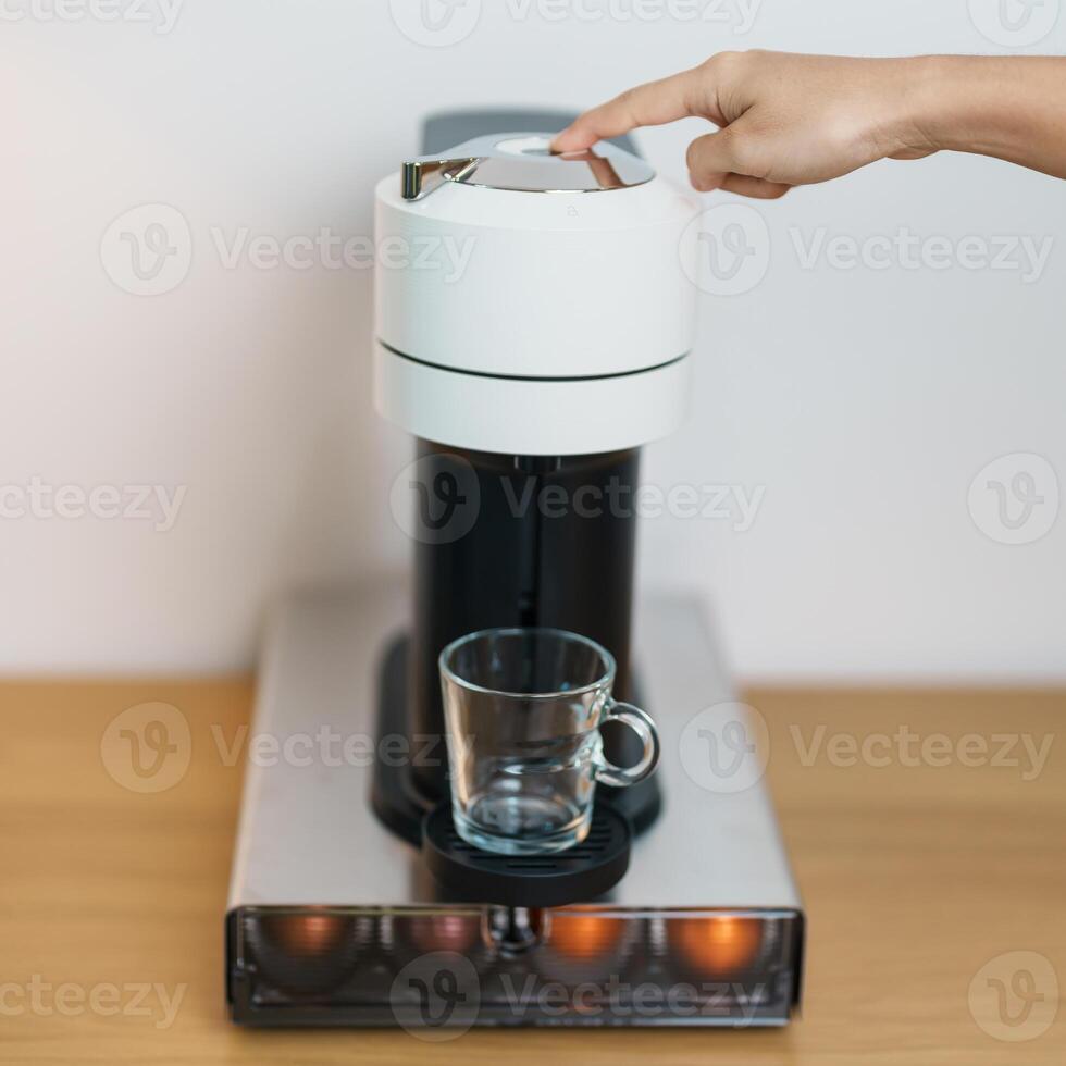 hand making Espresso Coffee by Coffee Maker Machine with Capsule of roasted coffee bean on wood table bar. Daily beverage drink at Home, Apartment and Office concept photo