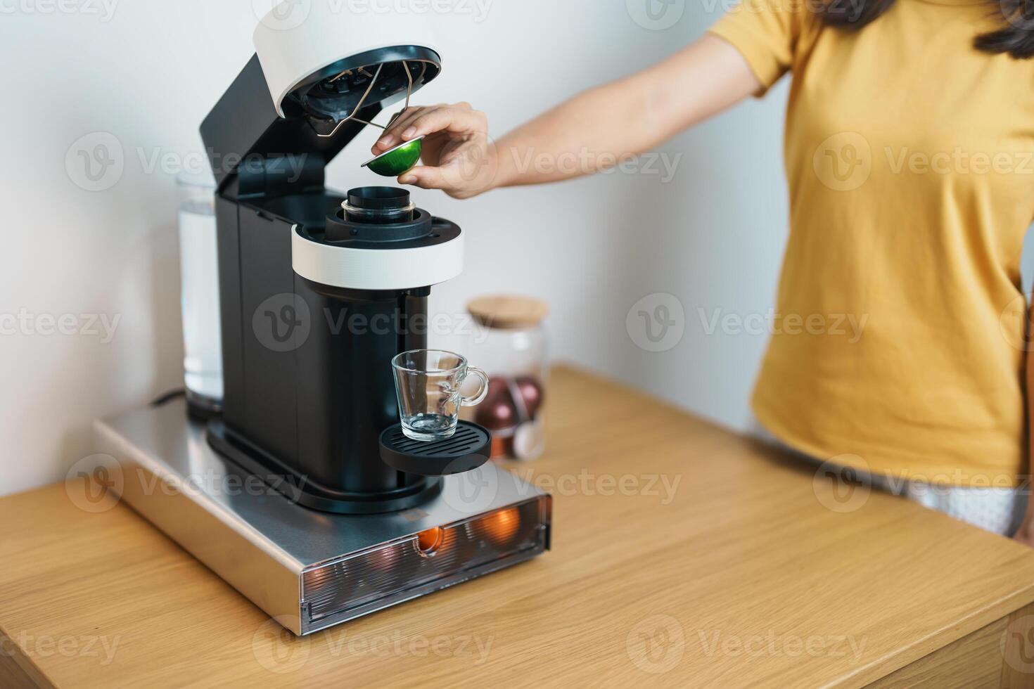 hand making Espresso Coffee by Coffee Maker Machine with Capsule of roasted coffee bean on wood table bar. Daily beverage drink at Home, Apartment and Office concept photo