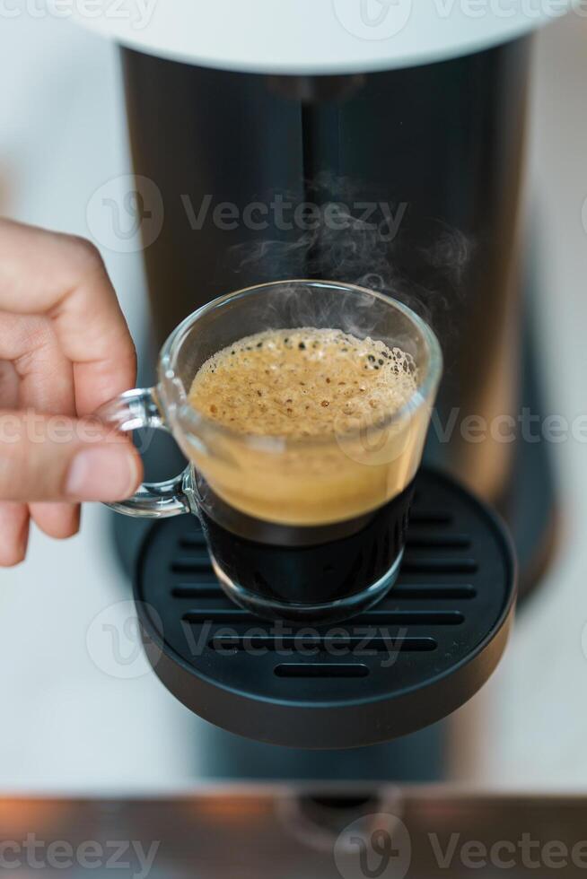 hand making Espresso Coffee by Coffee Maker Machine with Capsule of roasted coffee bean on wood table bar. Daily beverage drink at Home, Apartment and Office concept photo