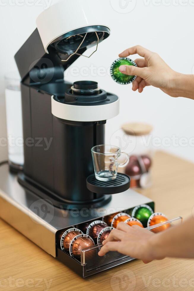hand making Espresso Coffee by Coffee Maker Machine with Capsule of roasted coffee bean on wood table bar. Daily beverage drink at Home, Apartment and Office concept photo