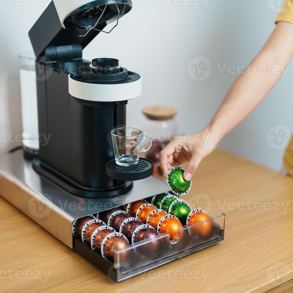 hand making Espresso Coffee by Coffee Maker Machine with Capsule of roasted coffee bean on wood table bar. Daily beverage drink at Home, Apartment and Office concept photo