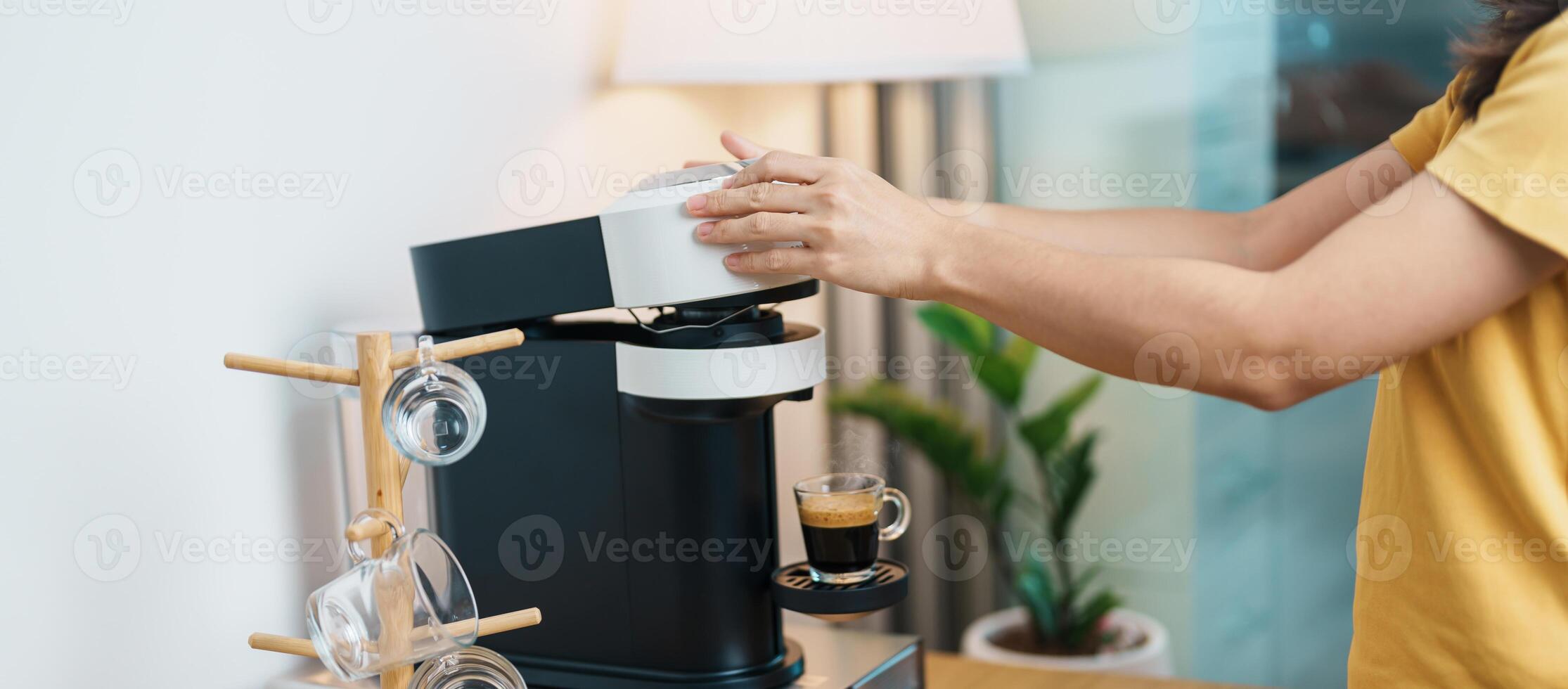 hand making Espresso Coffee by Coffee Maker Machine with Capsule of roasted coffee bean on wood table bar. Daily beverage drink at Home, Apartment and Office concept photo