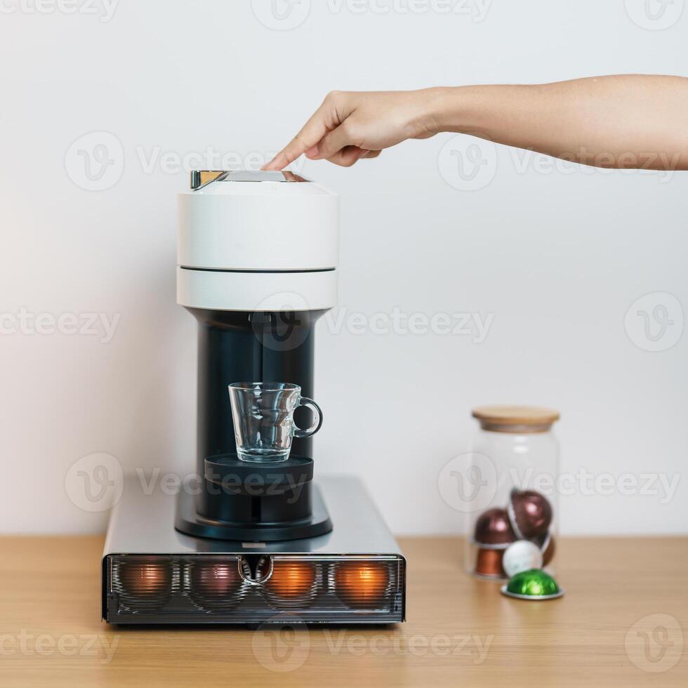 hand making Espresso Coffee by Coffee Maker Machine with Capsule of roasted coffee bean on wood table bar. Daily beverage drink at Home, Apartment and Office concept photo