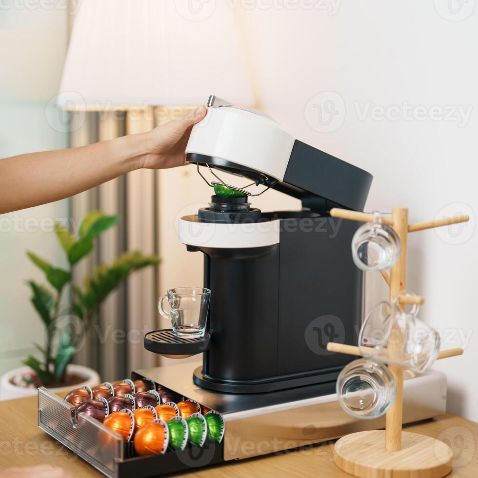 hand making Espresso Coffee by Coffee Maker Machine with Capsule of roasted coffee bean on wood table bar. Daily beverage drink at Home, Apartment and Office concept photo