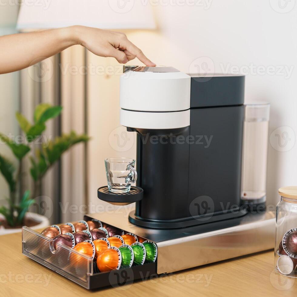 hand making Espresso Coffee by Coffee Maker Machine with Capsule of roasted coffee bean on wood table bar. Daily beverage drink at Home, Apartment and Office concept photo