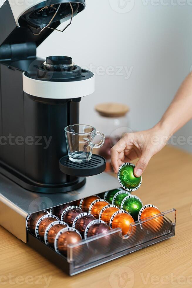 hand making Espresso Coffee by Coffee Maker Machine with Capsule of roasted coffee bean on wood table bar. Daily beverage drink at Home, Apartment and Office concept photo