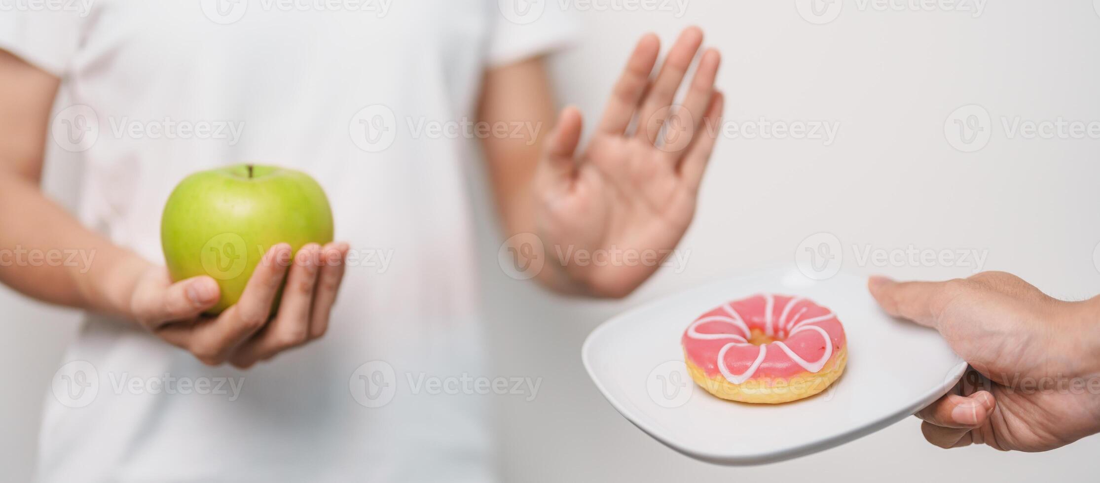 woman hand hold green Apple and reject donut, female fitness choose between fruit is Healthy and sweet is Unhealthy junk food. Dieting control, Weight loss, Obesity, eating lifestyle and nutrition photo
