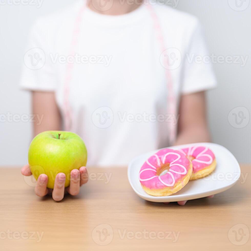 woman hand hold green Apple and donut, female fitness choose between fruit is Healthy and sweet is Unhealthy junk food. Dieting control, Weight loss, Obesity, eating lifestyle and nutrition concept photo