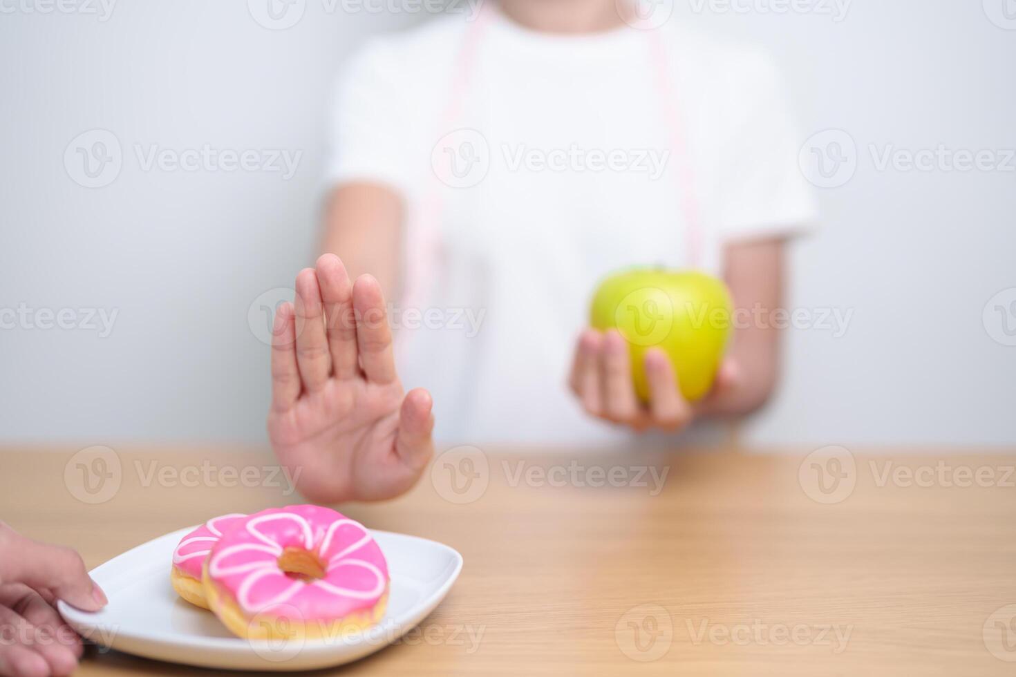 woman hand hold green Apple and reject donut, female fitness choose between fruit is Healthy and sweet is Unhealthy junk food. Dieting control, Weight loss, Obesity, eating lifestyle and nutrition photo