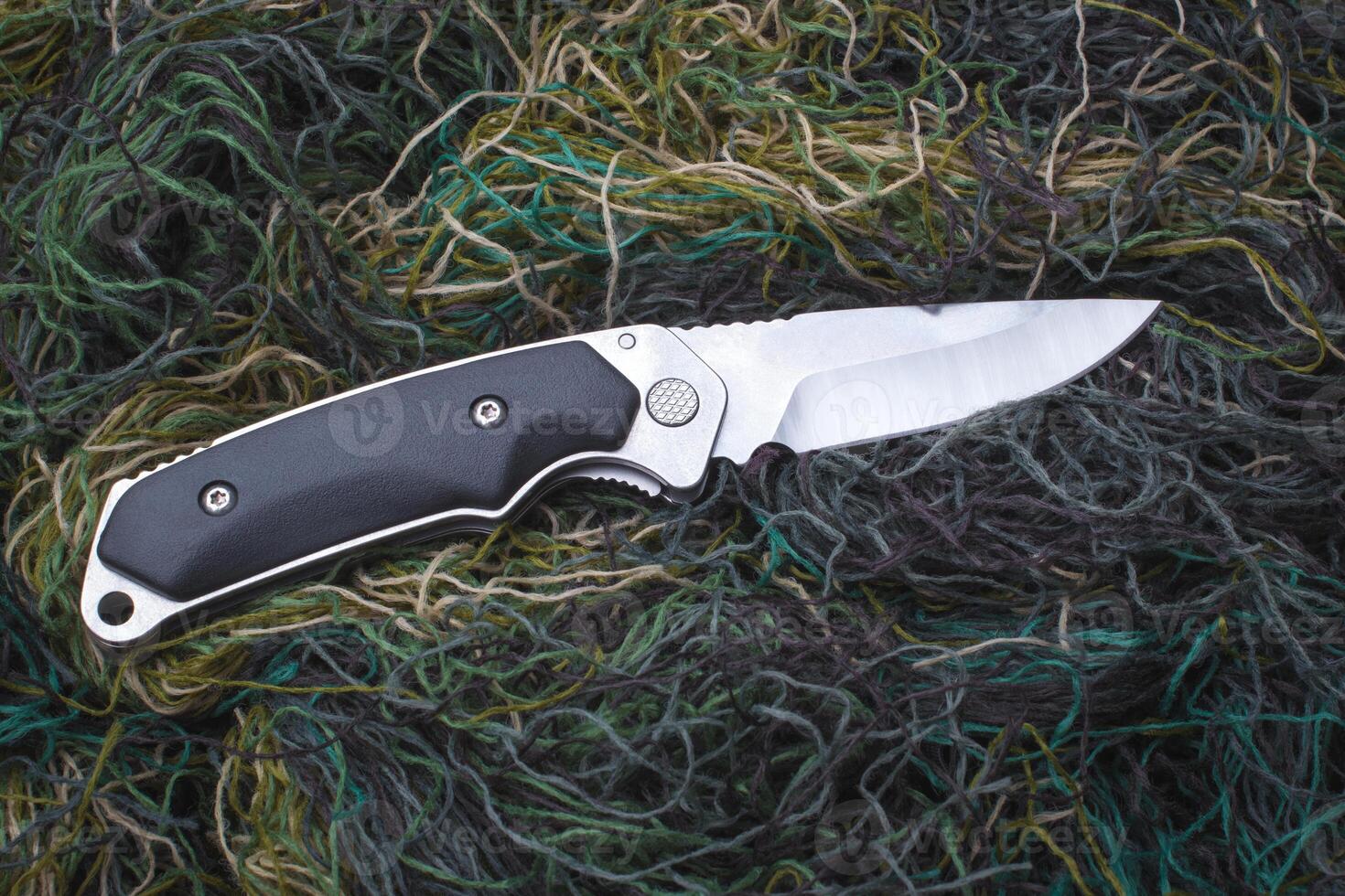 Folding penknife on the background of green threads. photo