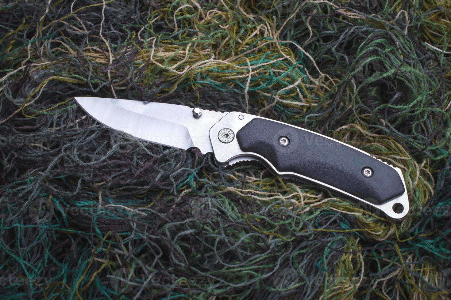 Folding penknife on the background of green threads. photo