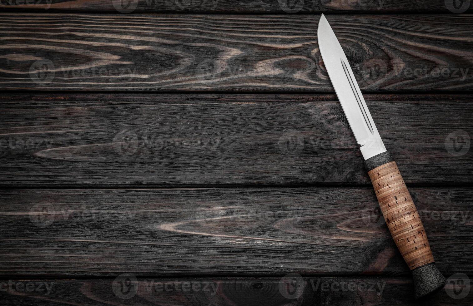 Hunting bowie knife with a wooden handle on dark wooden background. Steel arms weapon. top view photo