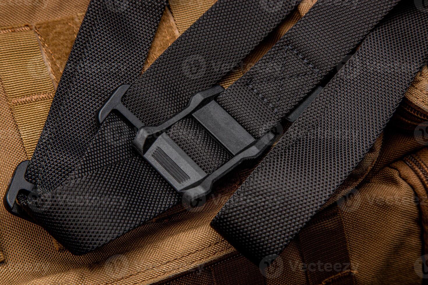 A black nylon weapon belt on a brown military backpack. Dark back. photo