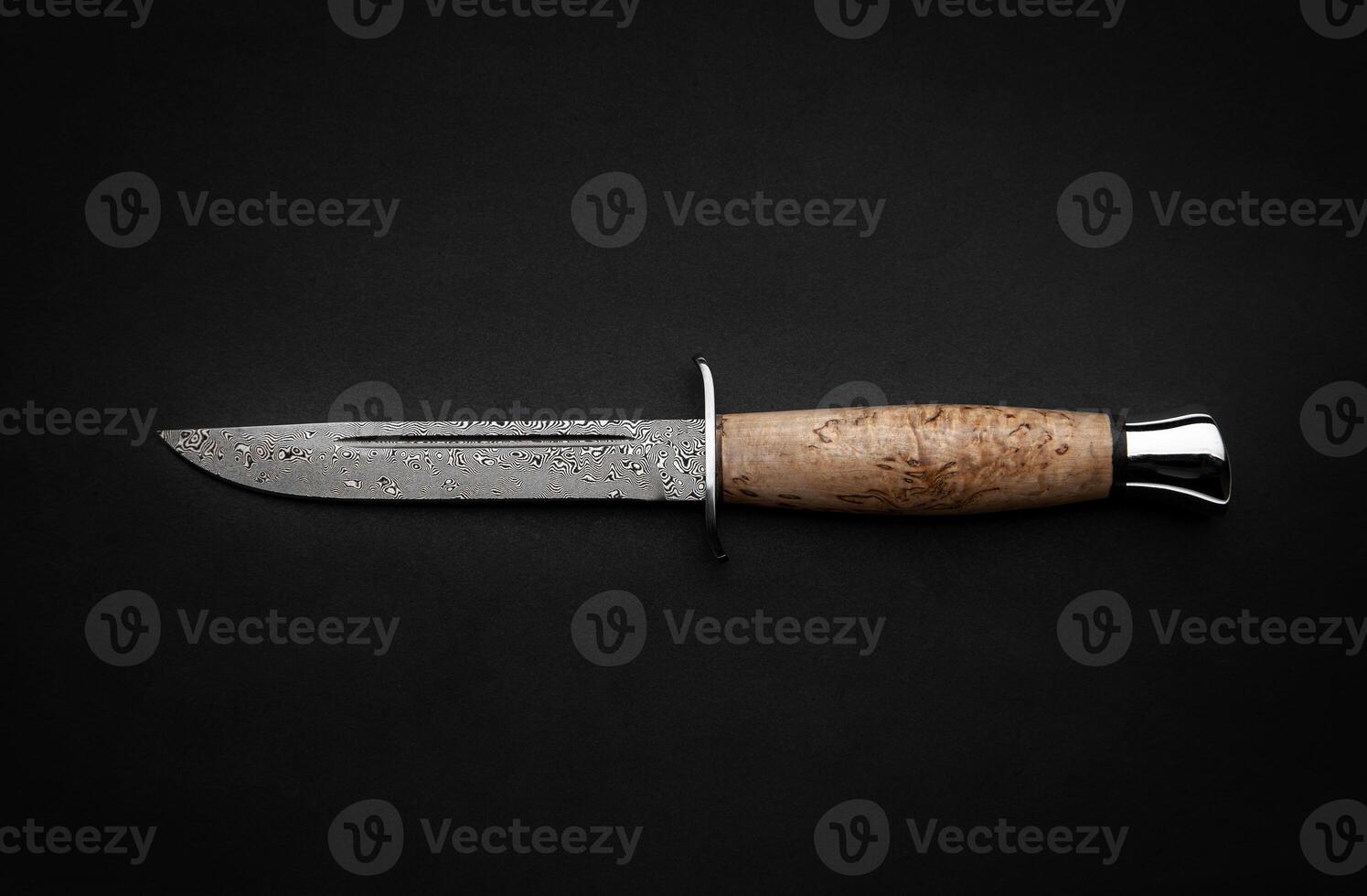 Damascus hunting knife with a wooden handle on a dark background. Melee weapons for hunting and self-defense. The instrument of crime. photo