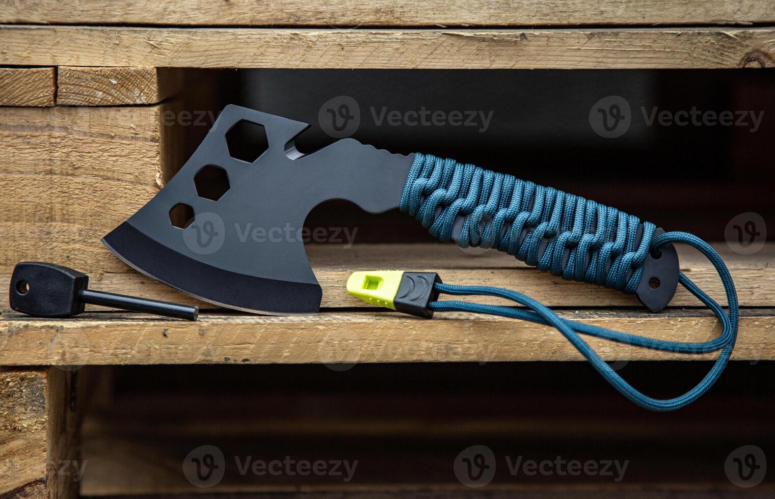 A small black ax with a paracord-wrapped handle. A tool for cutting branches or firewood in the forest. Self defense weapon. Wooden back. photo