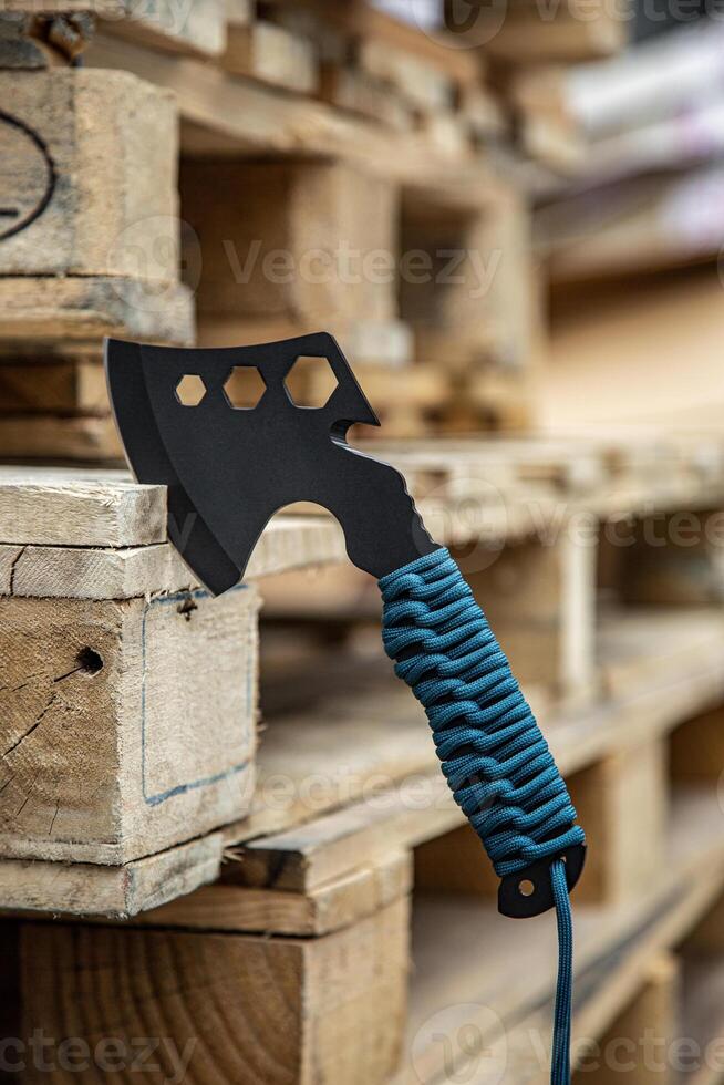 A small black ax with a paracord-wrapped handle. A tool for cutting branches or firewood in the forest. Self defense weapon. Wooden back. photo
