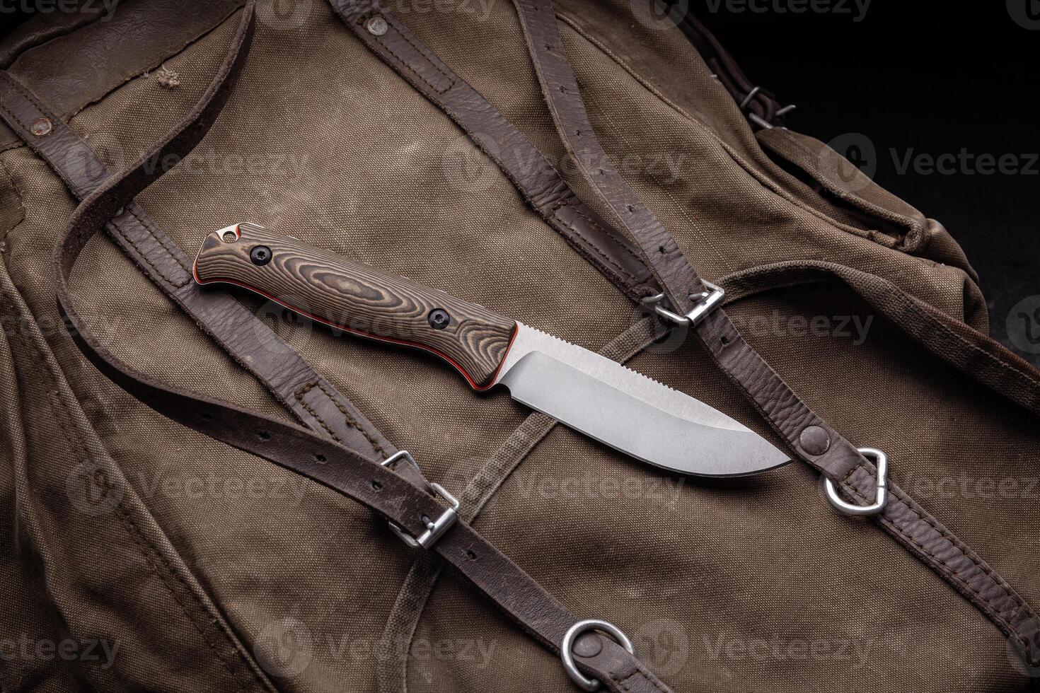 A hunting knife with a wooden handle on a khaki canvas backpack. Weapons for self-defense and survival. photo