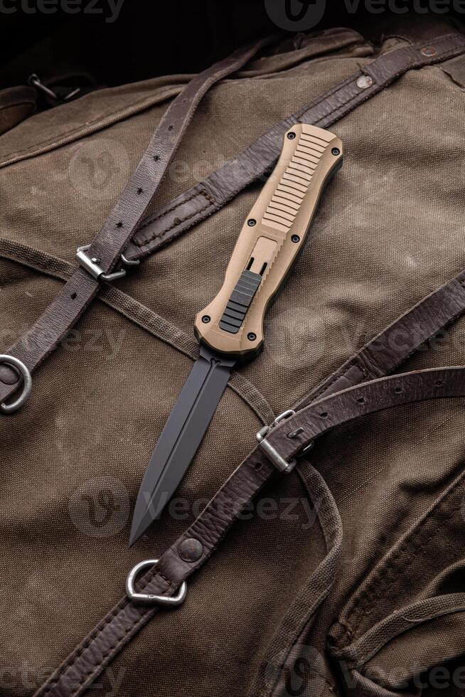 Modern folding knife on a rough canvas backpack. Melee weapons for self-defense and survival. A pocket knife on a rough dark back photo