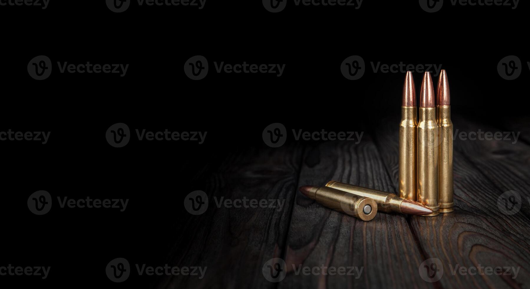 Carbine and rifle cartridges stand on a wooden surface. Ammunition for weapons. Dark back. photo