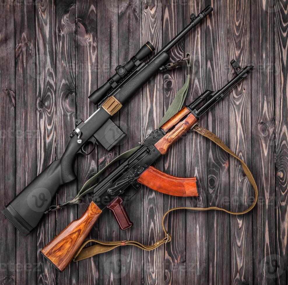 Two weapons lie on a plank surface. An old Soviet automatic carbine and a modern bolt-action rifle with a telescopic sight. Weapon on a wooden back photo