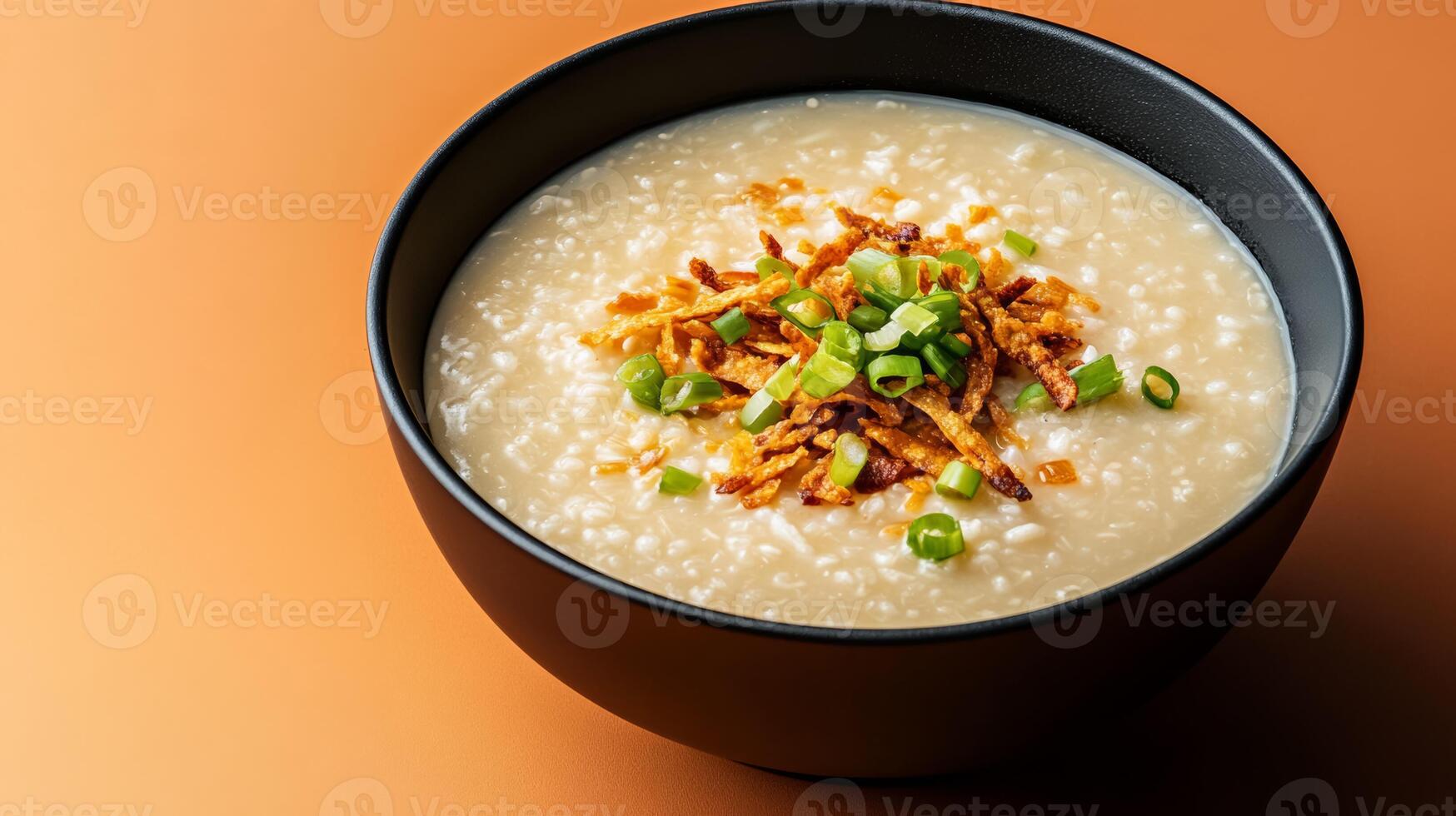 Warm autumn Asian dish featuring a bowl of savory pumpkin congee, topped with crispy shallots and fresh green onions, set against a gradient background shifting from burnt orange to deep brown photo