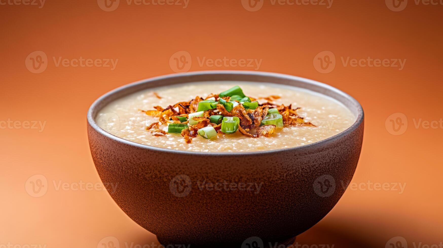 Warm autumn Asian dish featuring a bowl of savory pumpkin congee, topped with crispy shallots and fresh green onions, set against a gradient background shifting from burnt orange to deep brown photo