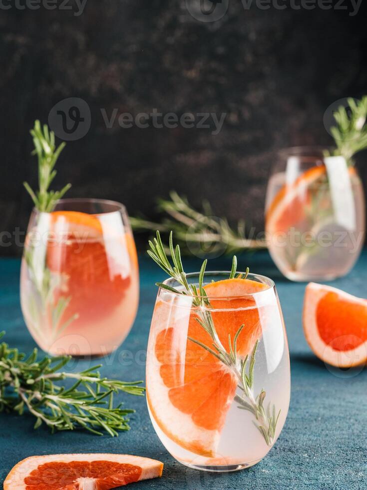infused detox water or alcoholic or non-alcoholic cocktail with grapefruit and rosemary in glass on green and black cement background. healthy eating or holyday drink concept, copy space for text photo