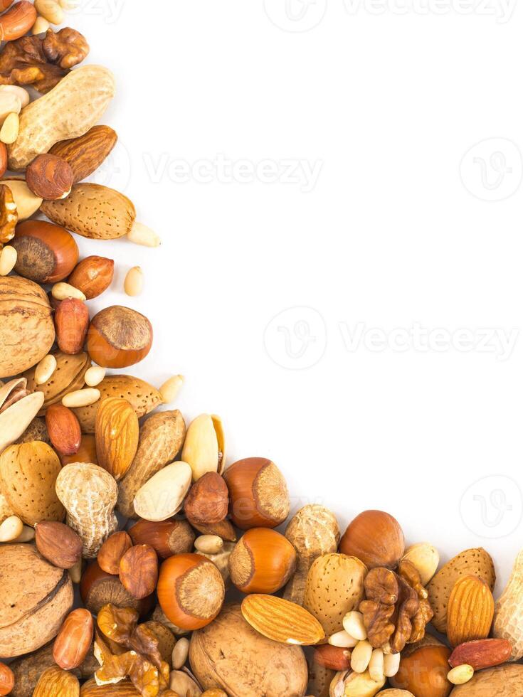 Background of mixed nuts - hazelnuts, almonds, walnuts, pistachios, peanuts, pine nuts peeled and not peeled - vertical with copy space. Isolated one edge. Top view or flat lay photo