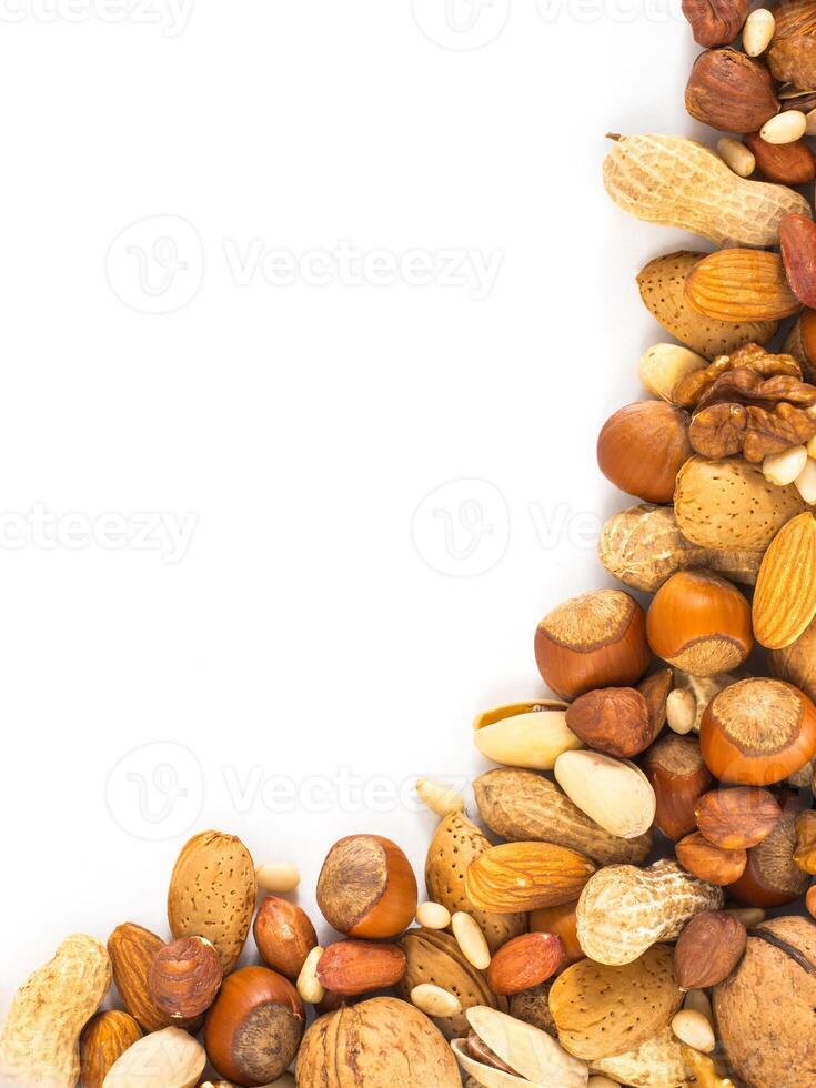 Background of mixed nuts - hazelnuts, almonds, walnuts, pistachios, peanuts, pine nuts peeled and not peeled - vertical with copy space. Isolated one edge. Top view or flat lay photo