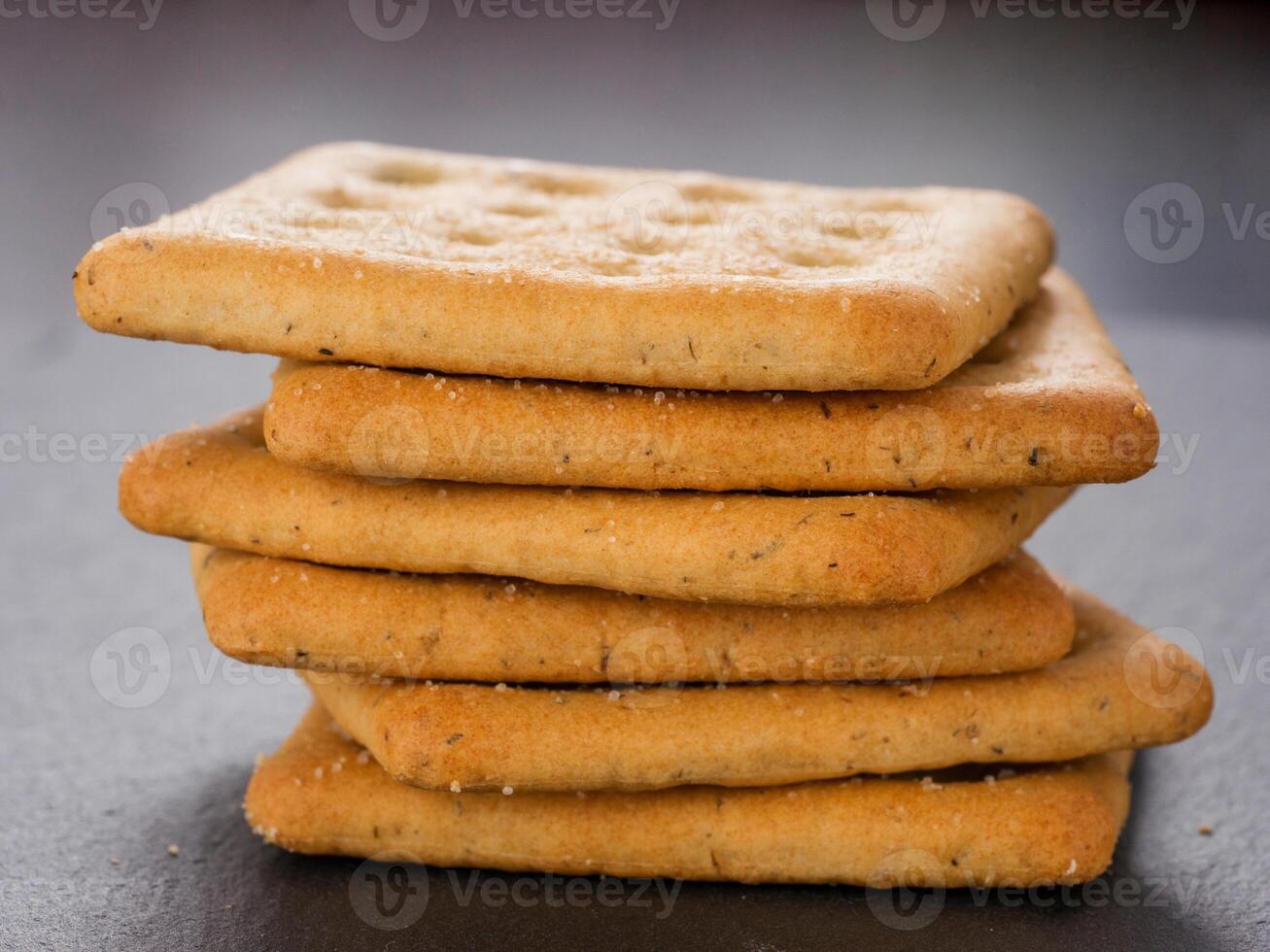 stack of square crackers on slate gray background. Dry salt cracker cookies with fiber and dry spices photo