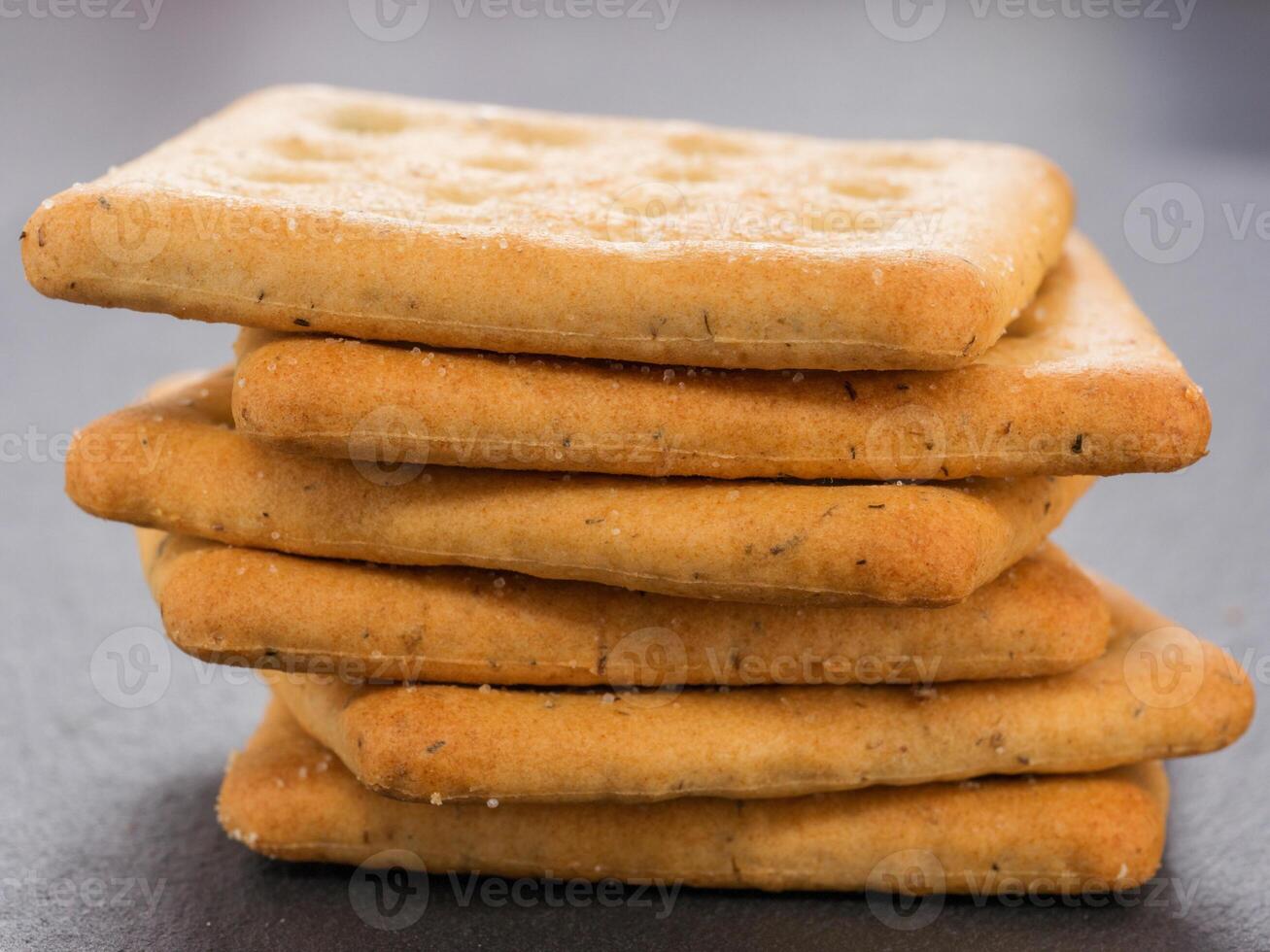 stack of square crackers on slate gray background. Dry salt cracker cookies with fiber and dry spices photo