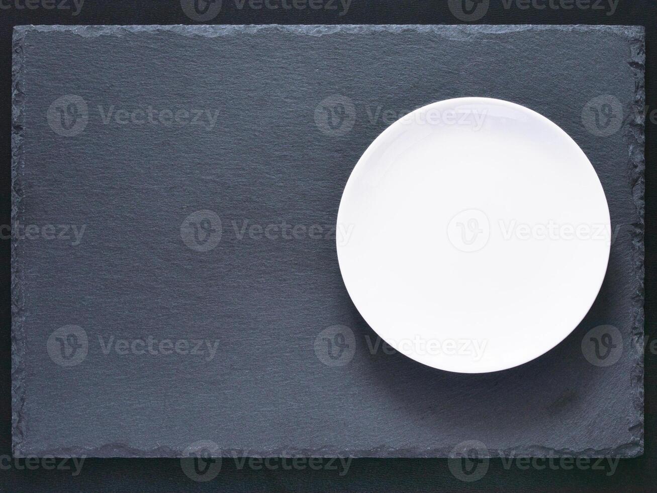 Empty white plate on black slate board on dark background. Flat lay or top view. Can use fo design menu photo