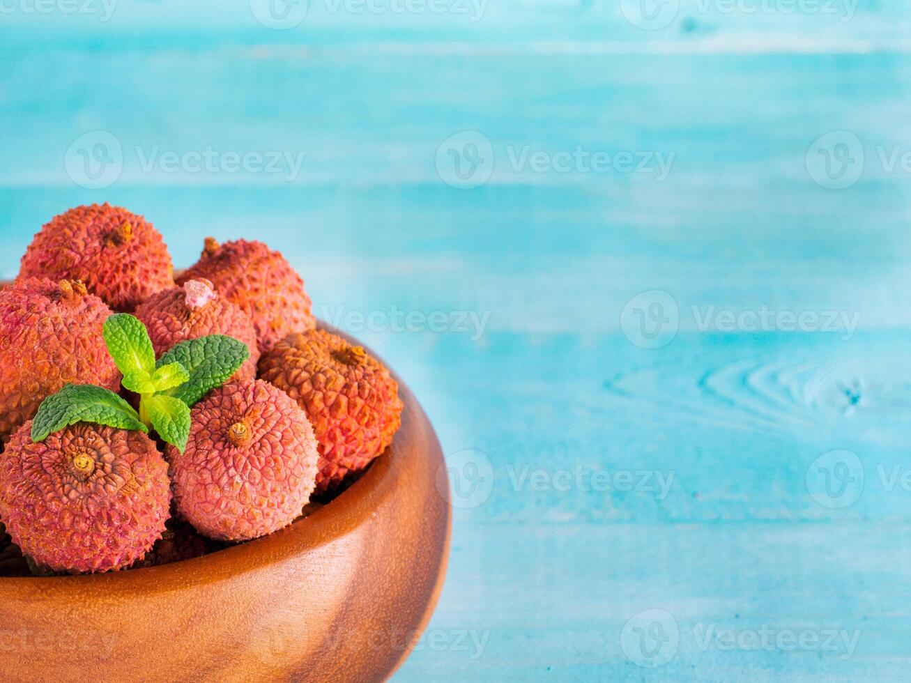 lychee fruit in clay plate on blue wooden background close up photo