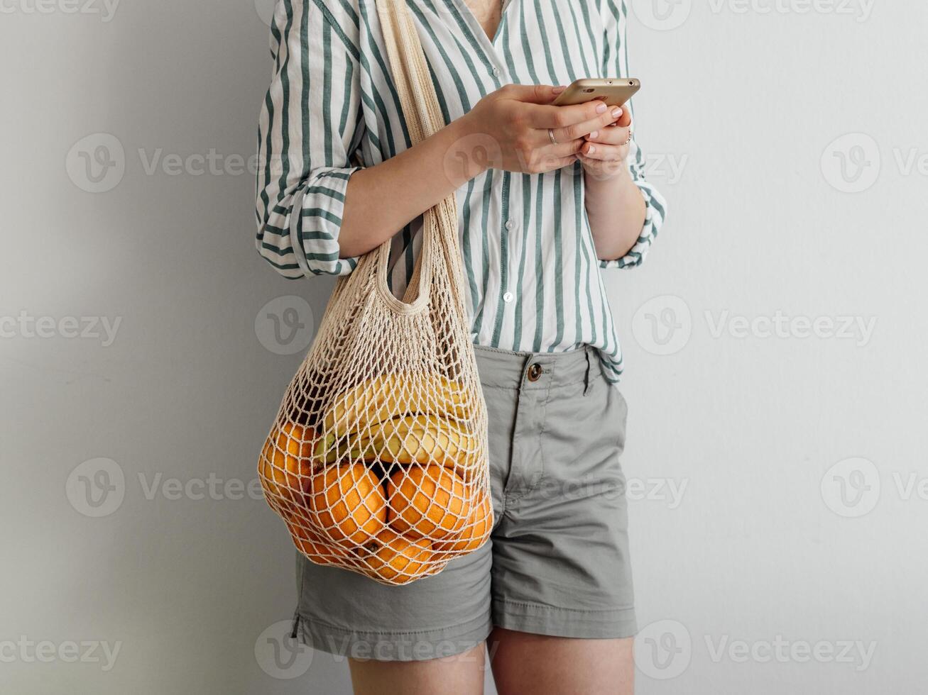 woman with mesh bag on shoulder using smartphone photo