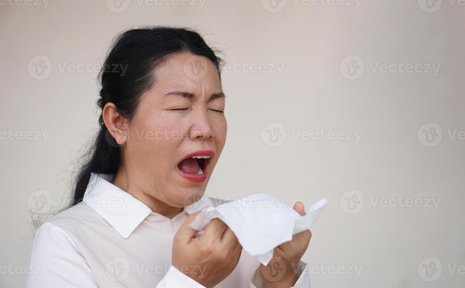 Asian woman is sneezing, open mouth, holds white tissue paper. Concept, Health problems. Ill, sick and flu. Cover mouth when cough or sneeze to stop spreading of germs, disease photo