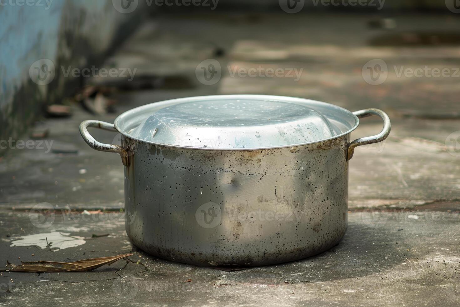 Old aluminum cooking pot sitting on a concrete floor photo