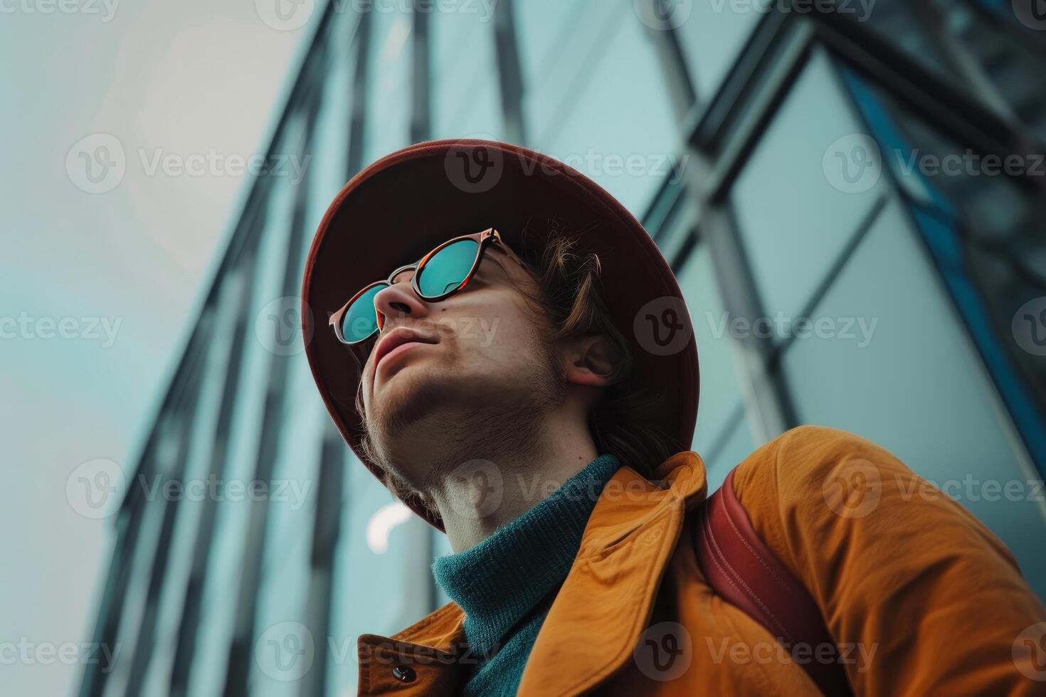 Stylish man wearing hat and sunglasses looking up at modern building photo