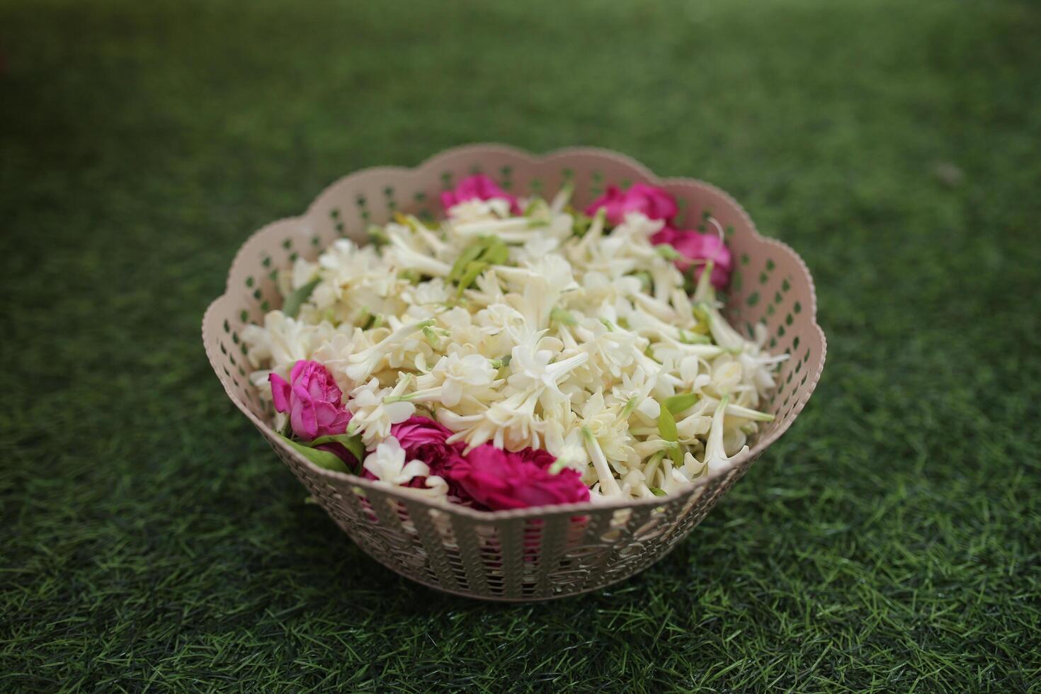 Polianthes tuberosa, and some pink rose cuttings in a bowl for a wedding event with a green grass background photo