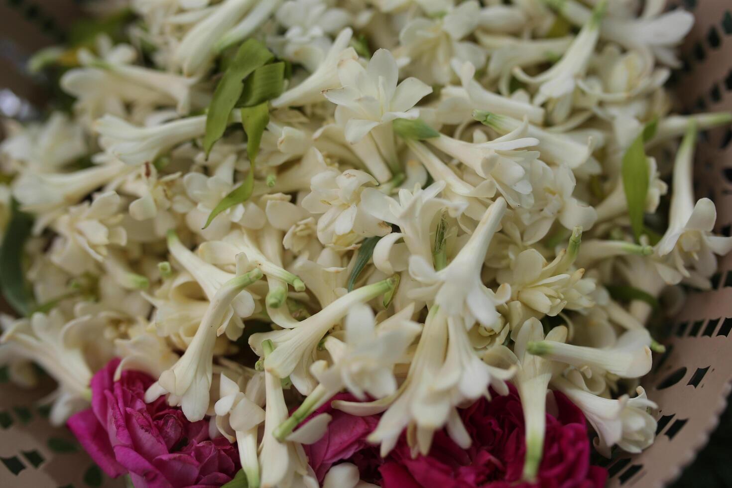 Polianthes tuberosa, and some pink rose cuttings in a bowl for a wedding event with a green grass background photo