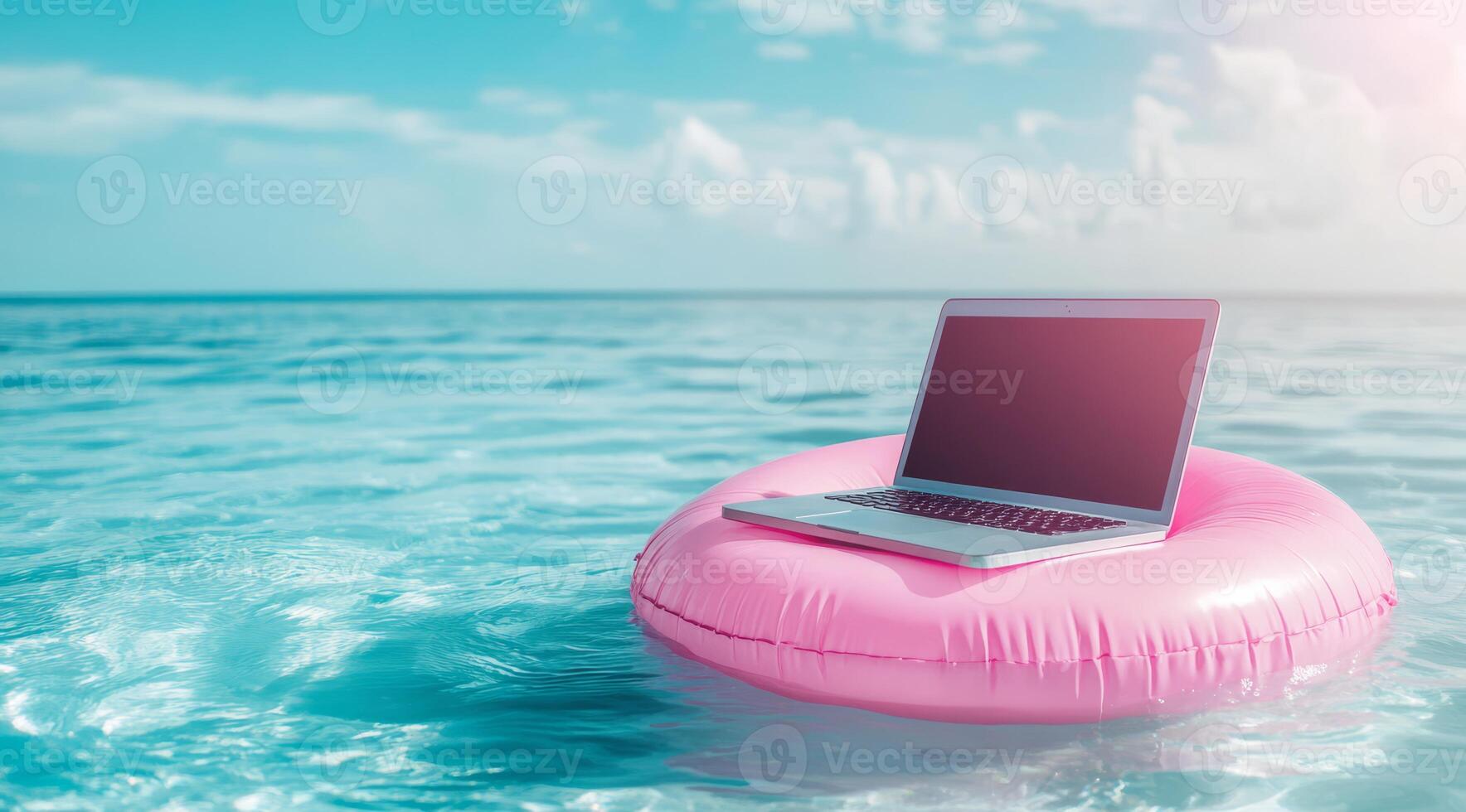 A laptop is precariously perched on a bright pink pool float, gently bobbing in the vast ocean, representing the perfect blend of work and relaxation that many modern workaholics seek photo