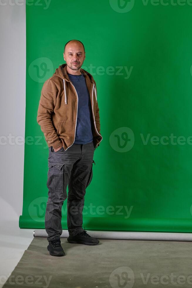 Middle aged bald man in casual attireposes confidently against a green studio backdrop. photo