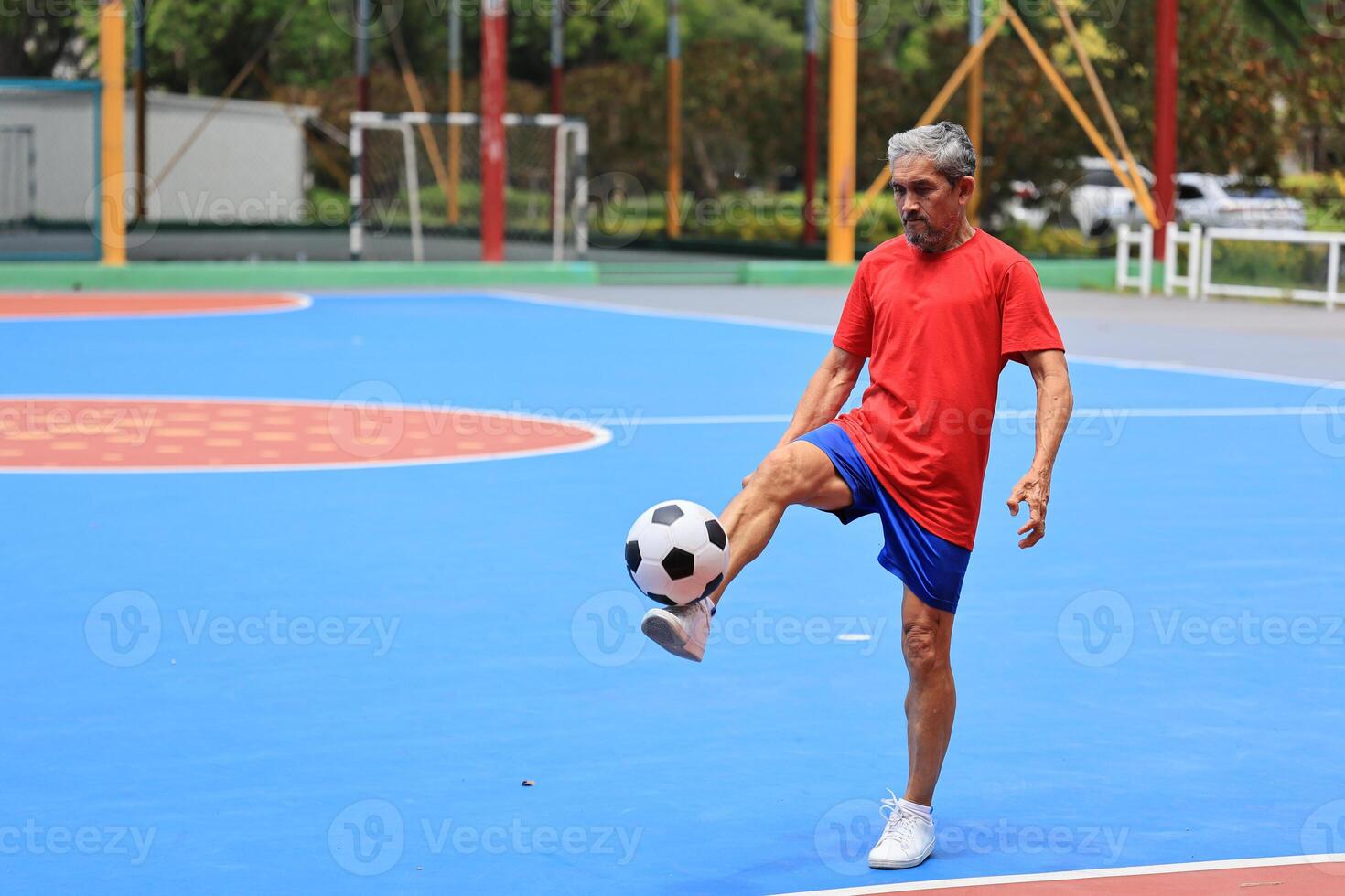 Senior Asian man in retirement age playing soccer football at outdoor court for healthy and fun activity to exercise and workout against aging illness photo