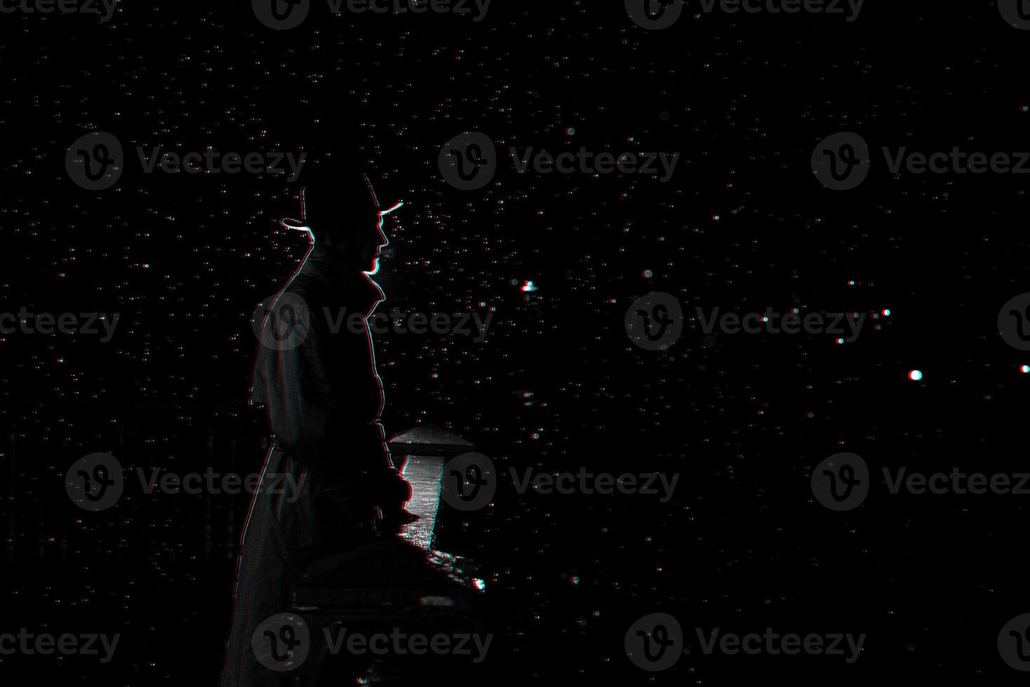 dark silhouette of a man in a hat at night in the rain in the city photo