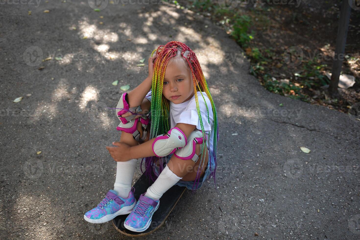 little cute girl with colorful afro pigtails sits on a skateboard photo