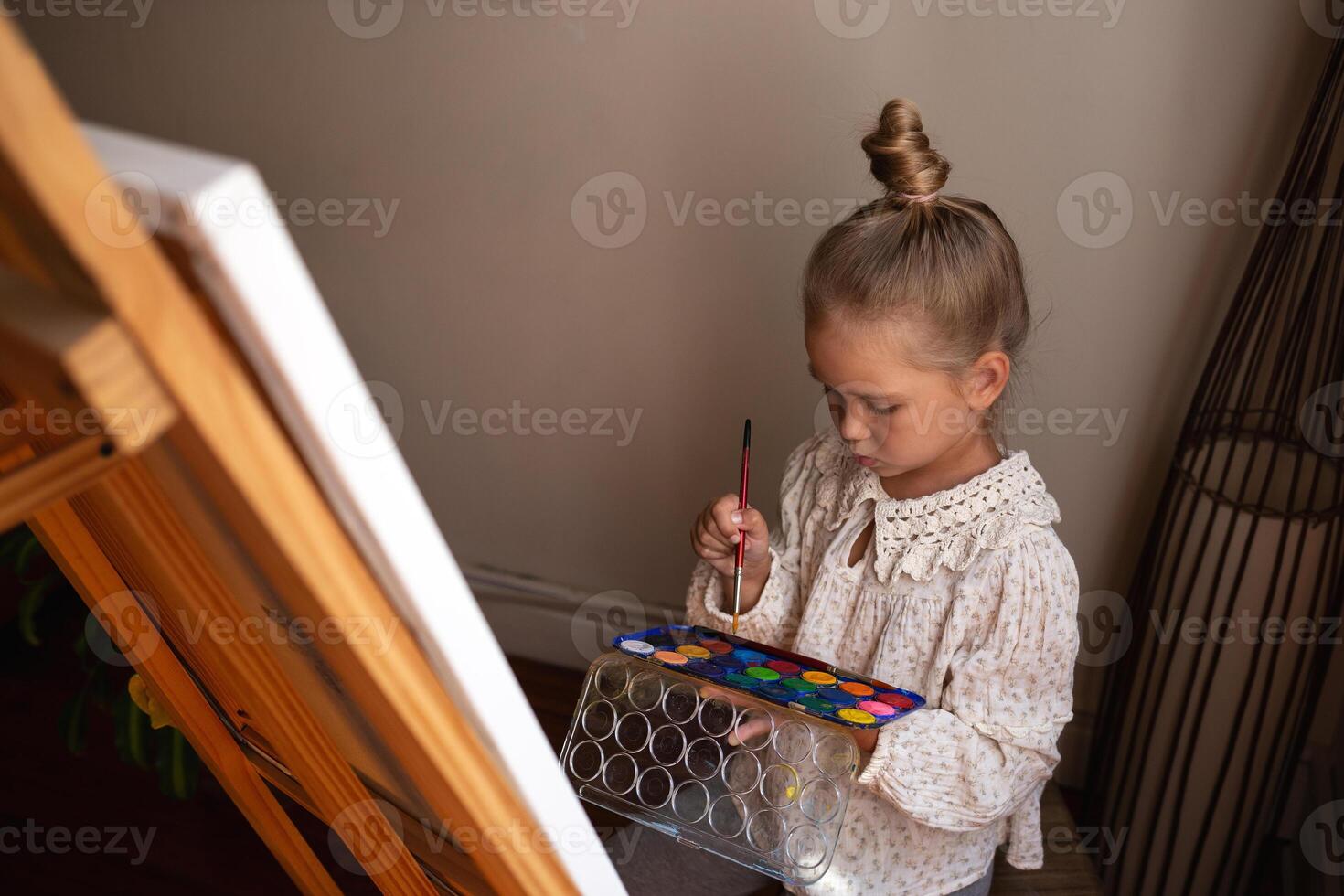 little cute girl draws with paints on canvas at the easel photo