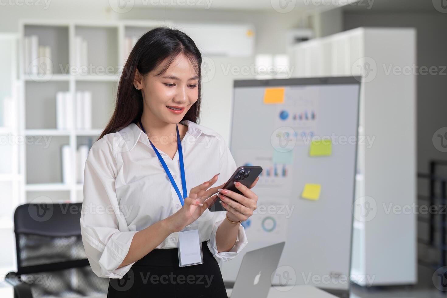 Young Accountant Using Smartphone in Modern Office Setting with Charts and Laptop in Background photo