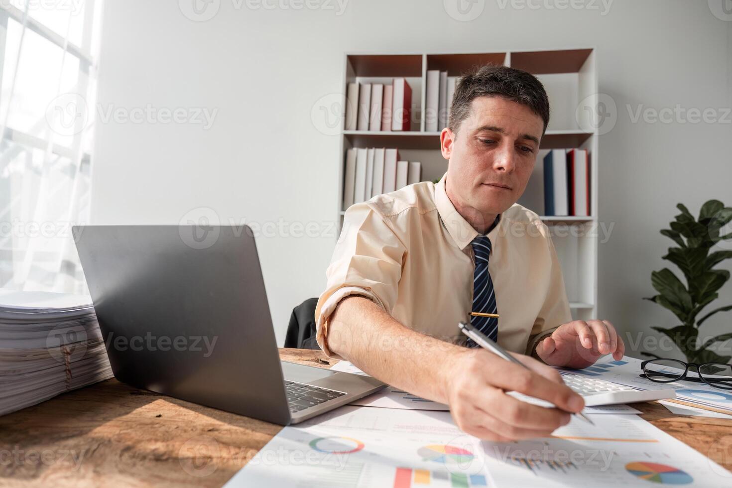 Focused Young Businessman Working at Office Desk with Laptop and Documents in Bright Modern Workspace photo
