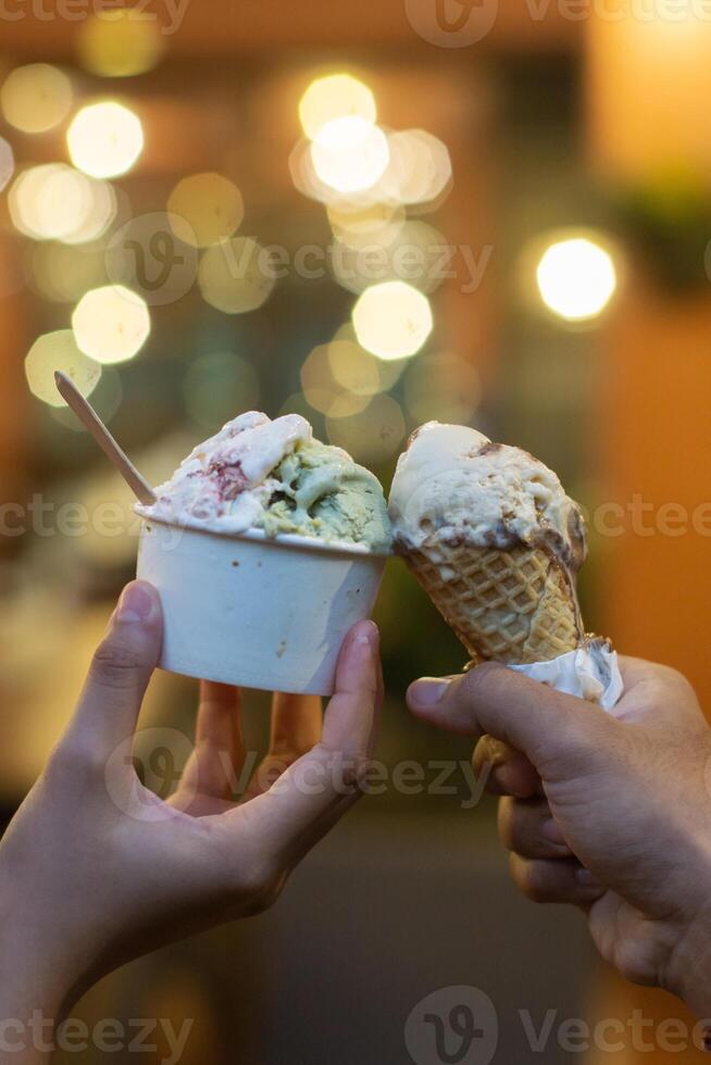 Close up hand of a person holding a cup and a cone of ice cream with blurred background photo