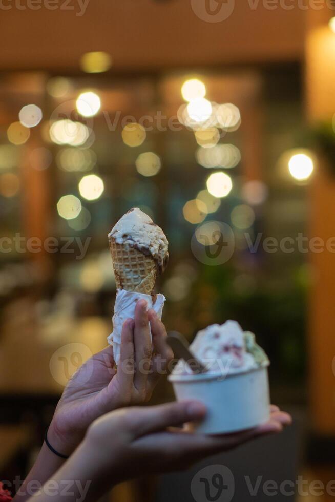 Close up hand of a person holding a cup and a cone of ice cream with blurred background photo