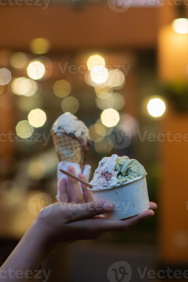 Close up hand of a person holding a cup and a cone of ice cream with blurred background photo